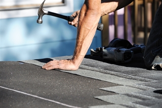 man hammering shingles on roof